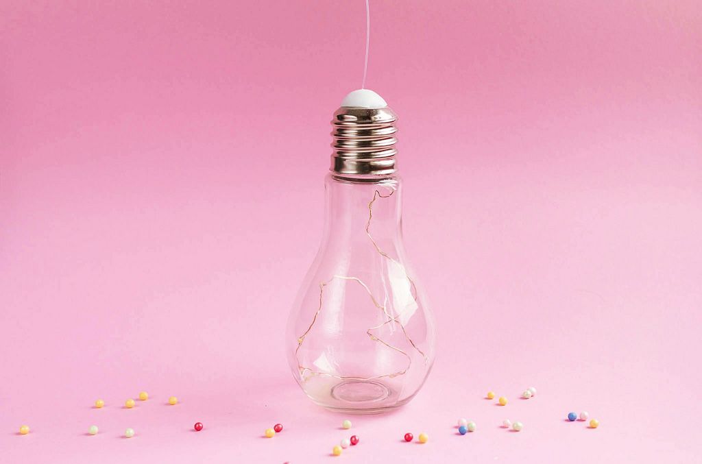 Stylish Big Bulb with lights inside on pink background. Colorful sprinkles