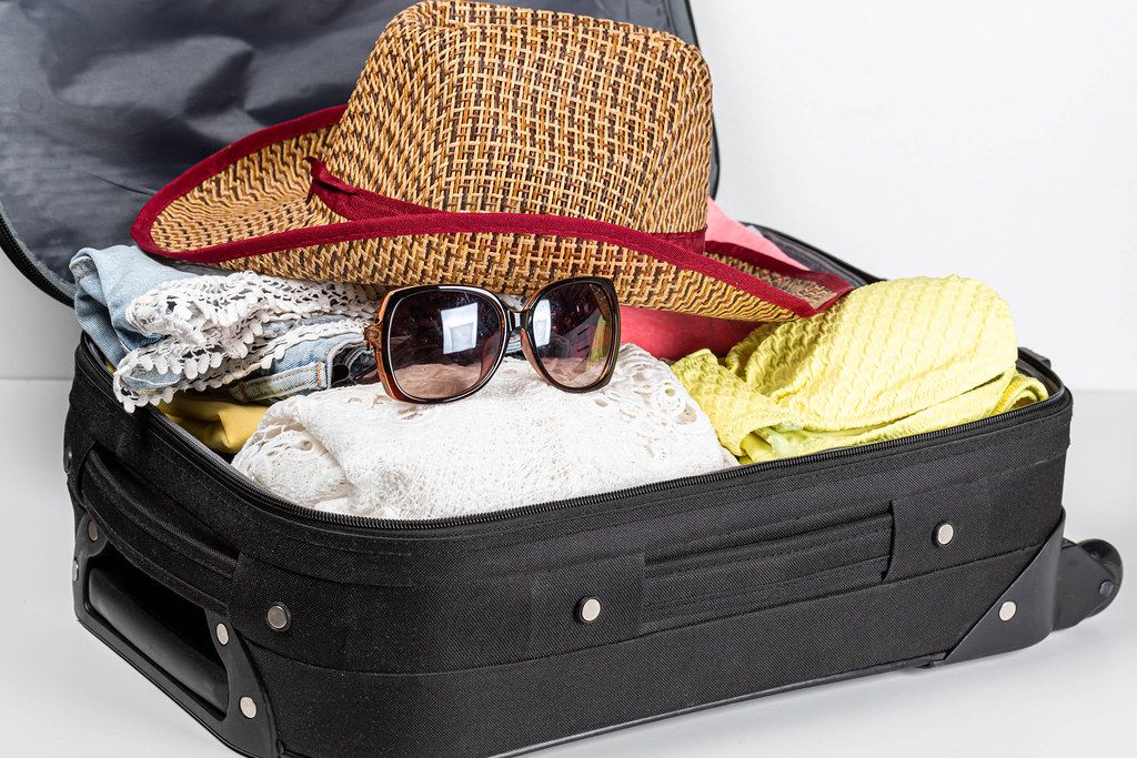 Suitcase preparation for a summer holiday with summer clothes, sunglasses and a hat