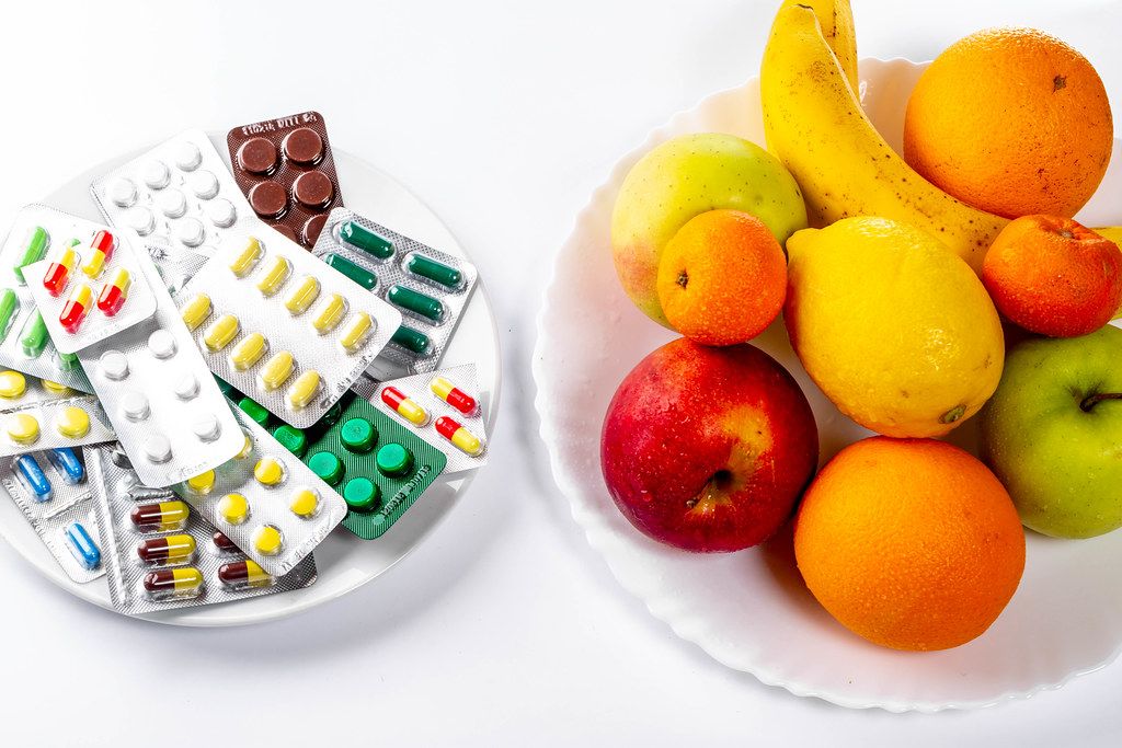 Tablets and fresh fruit on white background. The concept of choosing between a healthy diet and treatment (Flip 2019)