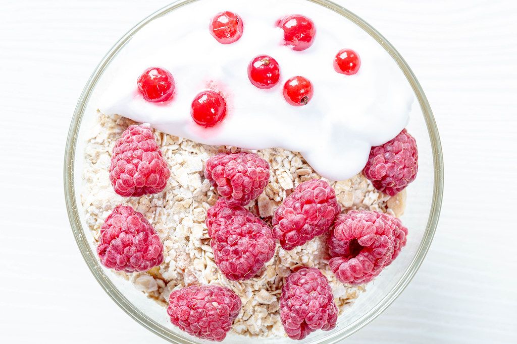 Tasty oatmeal porridge with raspberries and red currant, close up view