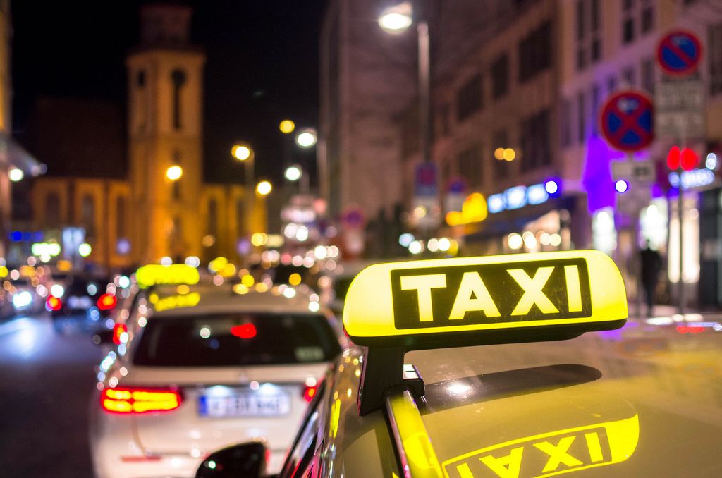 Taxis fahren bei Nacht durch Stadt – im Fokus Taxischild auf Autodach, Stadt mit Bokeh