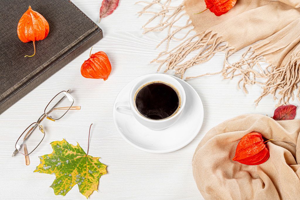 The concept of rest in the autumn season. A Cup of hot coffee with a closed book, glasses and a maple leaf (Flip 2019)