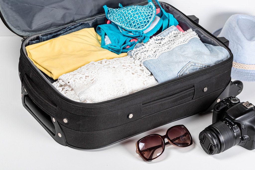 The concept of summer holidays and travel. Suitcase with clothes and camera on a white background