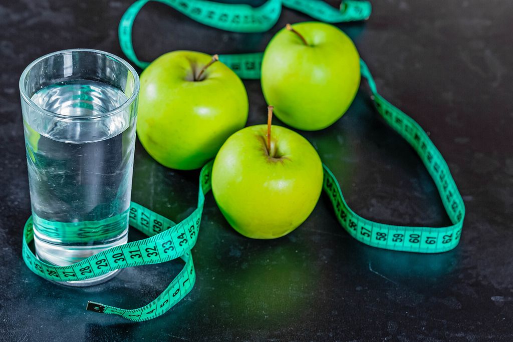 The concept of weight loss: the green apples and a glass of water with a measuring tape on black background