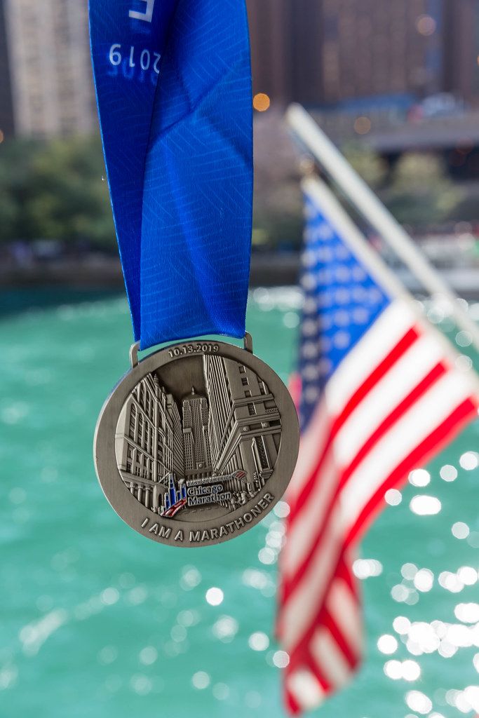 The medal given to a participant who completed the Chicago Marathon 2019, with a blue ribbon, the American flag and the Chicago River in the background