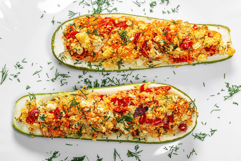 Top view baked zucchini halves with vegetables, couscous and herbs