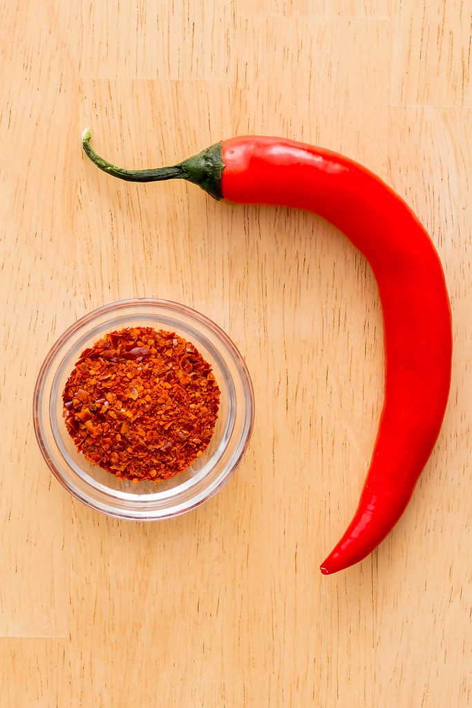 Top View Close Up Photo of Red Chili Pepper next to a small Bowl of Chili Powder on Wooden Background