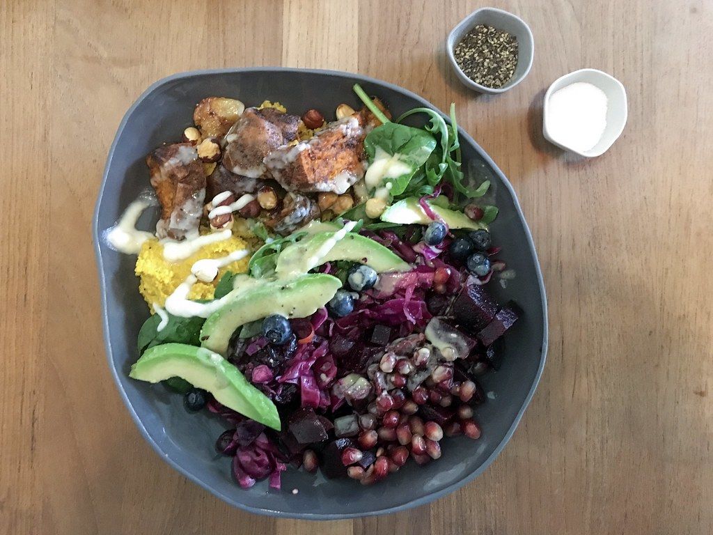 Top View Food Photo of Healthy Vegan Rainbow Bowl with Sweet Potato, Avocado, Pomegranate, Red Cabbage and Blueberries on Wooden Table