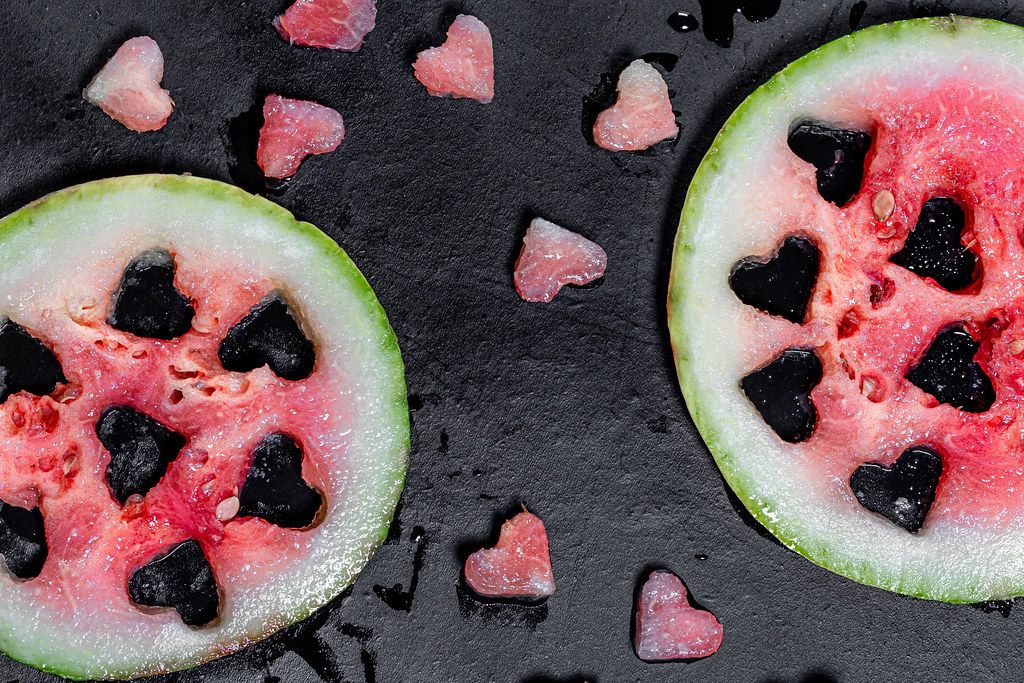 Top view fresh watermelon with cut heart shaped pieces on black background