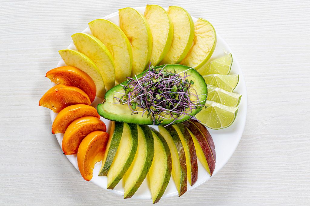 Top view fruit slicing on a white plate with avocado and micro green cabbage in the middle