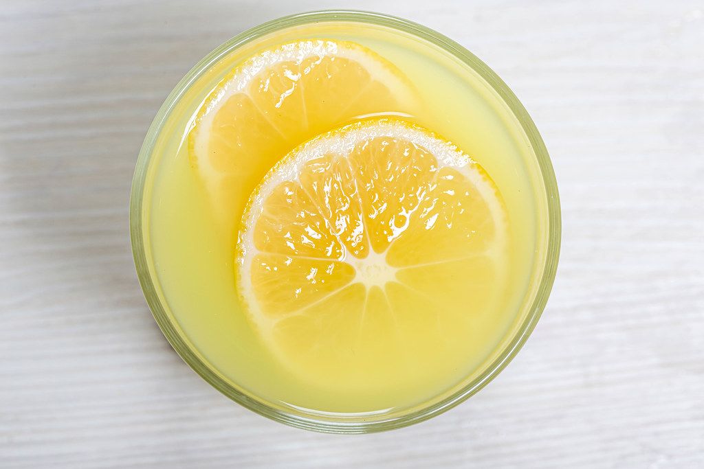 Top view glass of lemon juice with a slice of lemon on white wooden background