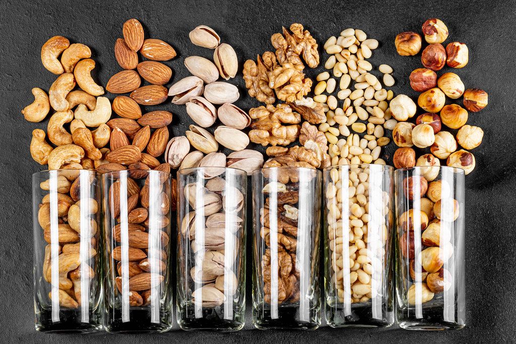 Top view, glasses with pistachios, almonds, cashews, walnuts, pine nuts and hazelnuts on a black background
