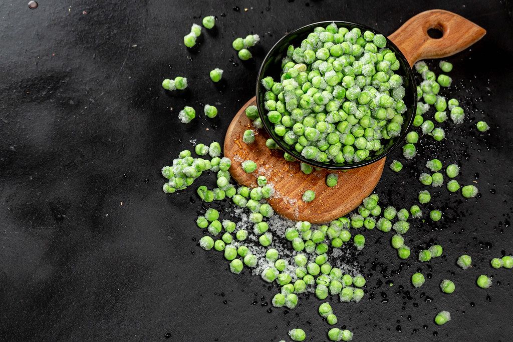 Top view green young peas in a bowl and scattered on a black background