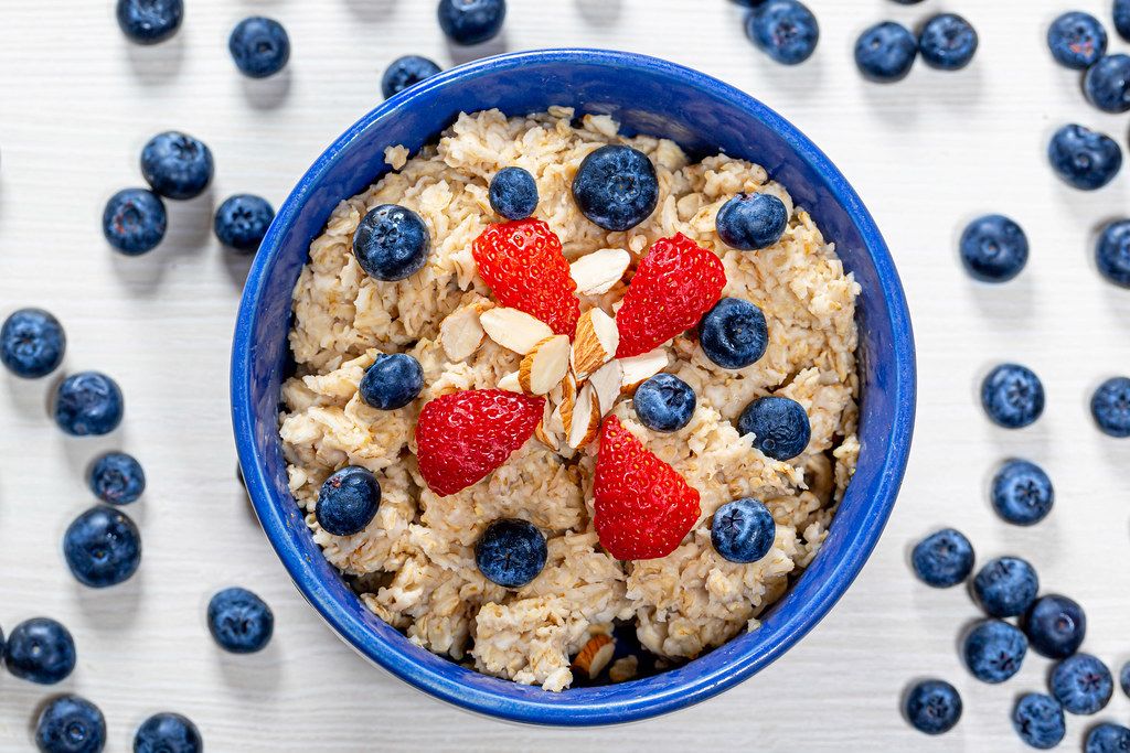 Top view oatmeal porridge with blueberries, almonds and strawberries on a white wooden background