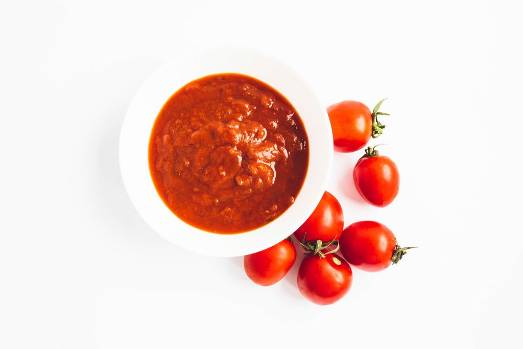 Top view of chopped tomatoes sauce in a bowl and fresh cherry tomatoes on white background