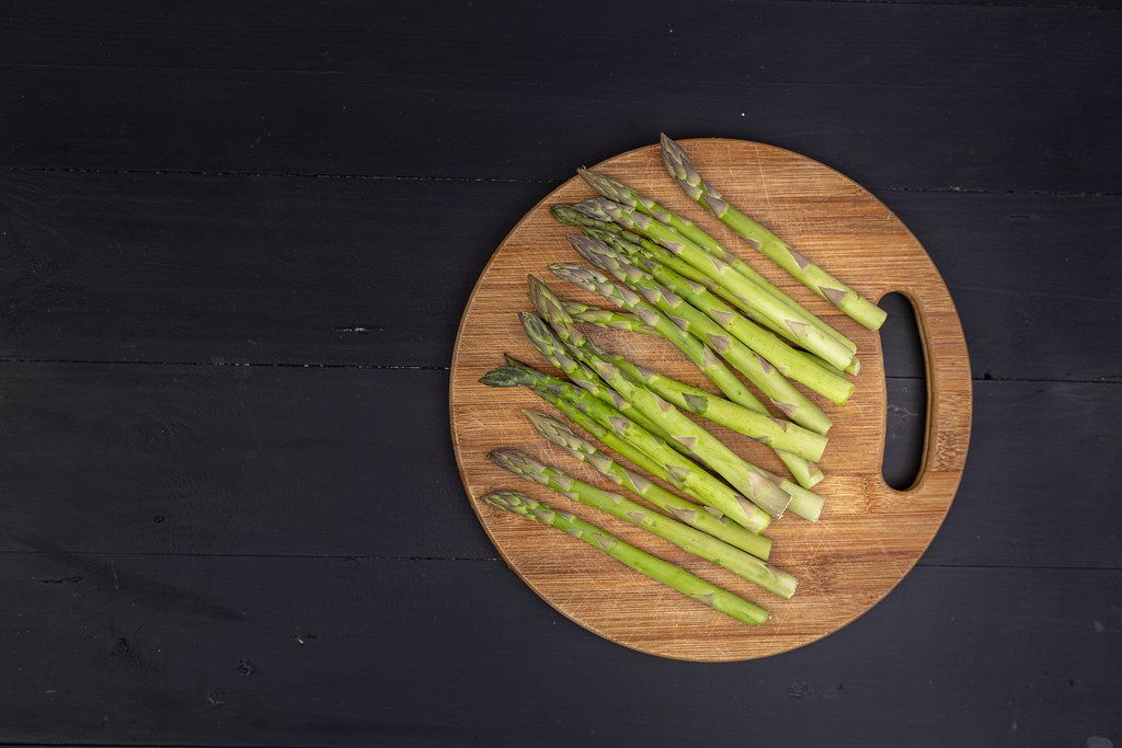 Top view of Fresh Asparagus on the round wooden board with black background with copy space