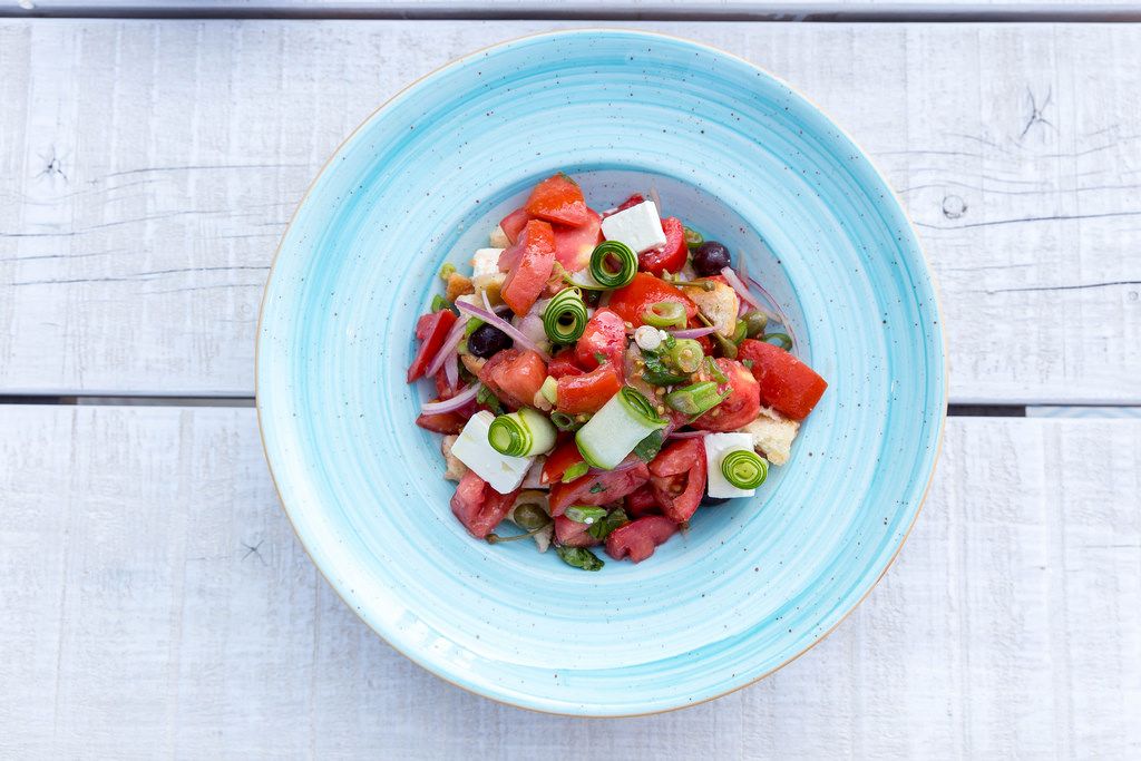 Top view of Greek salad with tomato, cucumber, dry onion, sun-dried tomato, feta cheese, capers and olive oil