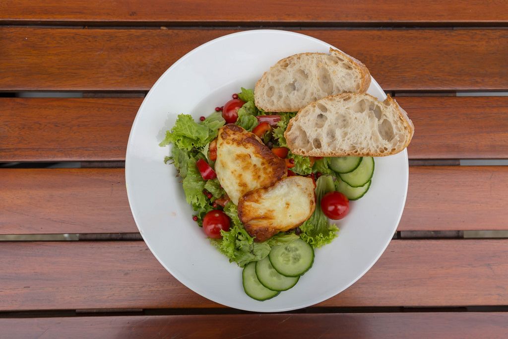Top view of mixed salad with cucumber, cherry tomato, halloumi cheese and two slices of bread