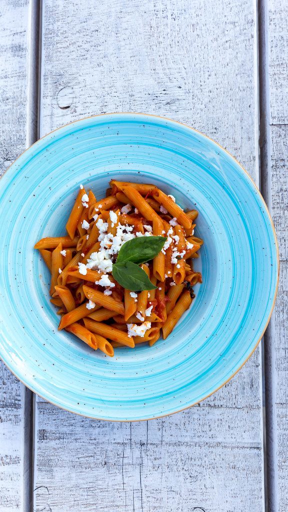 Top view of penne pasta with tomato sauce and grated feta cheese