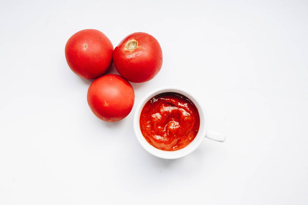 Top view of tomato sauce in a cup and tomatoes around. White background