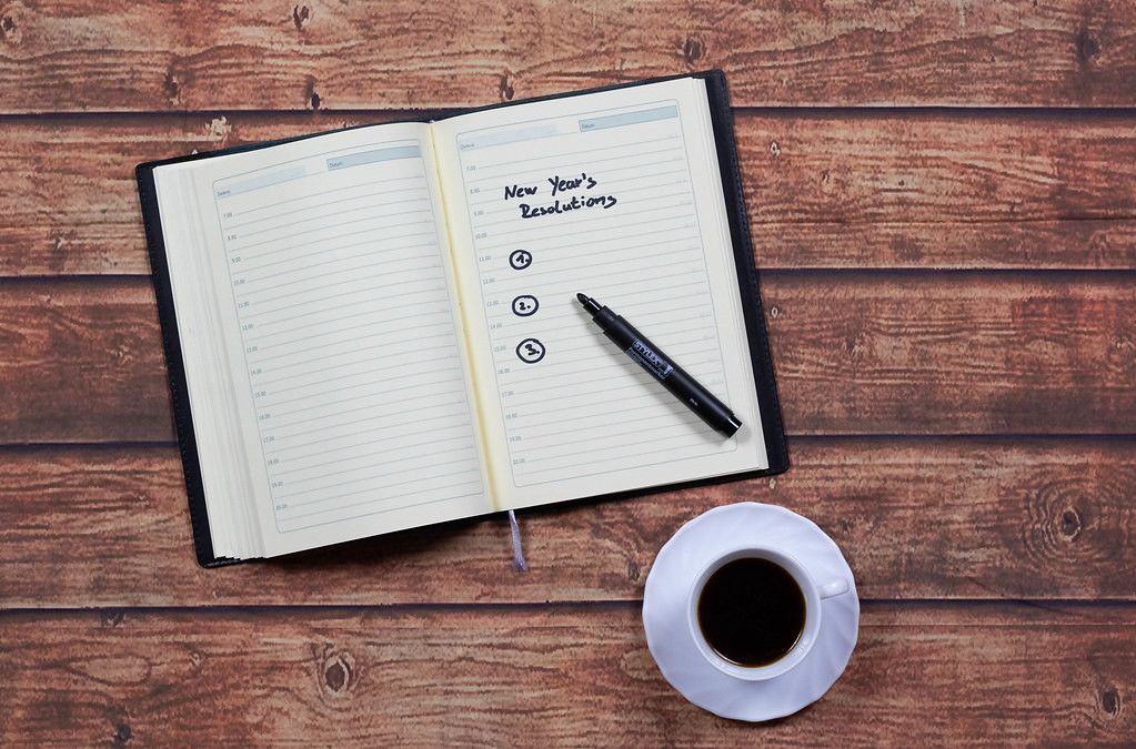 Top View Photo of Open Note Book with New Year's Resolution List next to a Cup Of Coffee on a Wooden Table