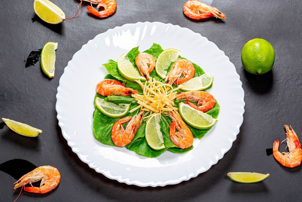 Top view salad with shrimp and slices of line on a black background