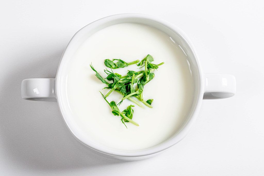 Top view white mushroom soup with micro greenery in tureen