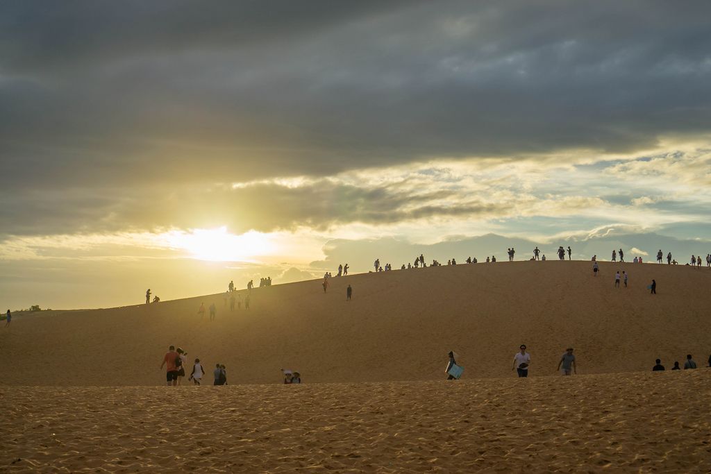 Touristen sehen sich den Sonnenuntergang über Mui Ne, Vietnam von den roten Sanddünen aus an