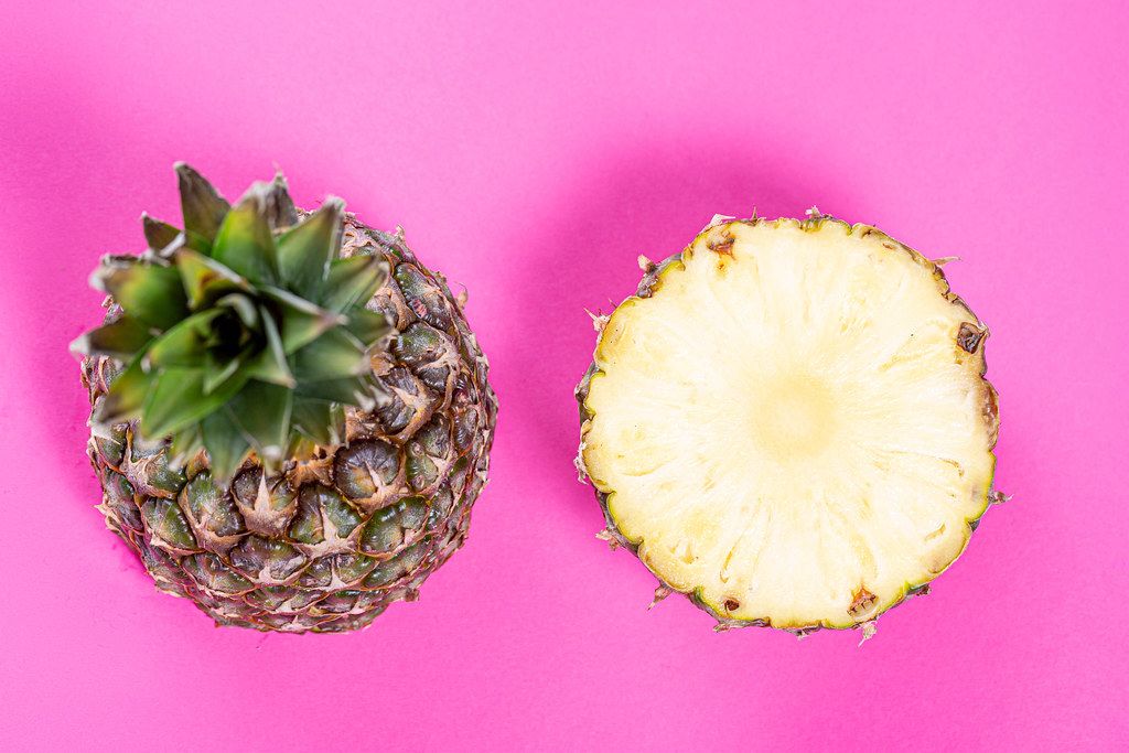 Two halves of a ripe pineapple on a pink background