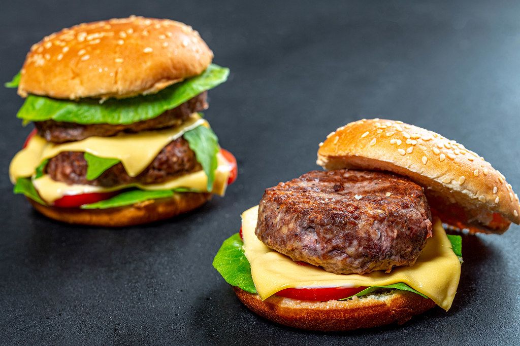 Two homemade Burger with beef patties, cheese and vegetables on black background (Flip 2019)