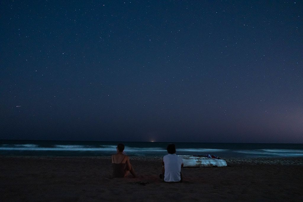 Two people on the beach watching stars above the sea