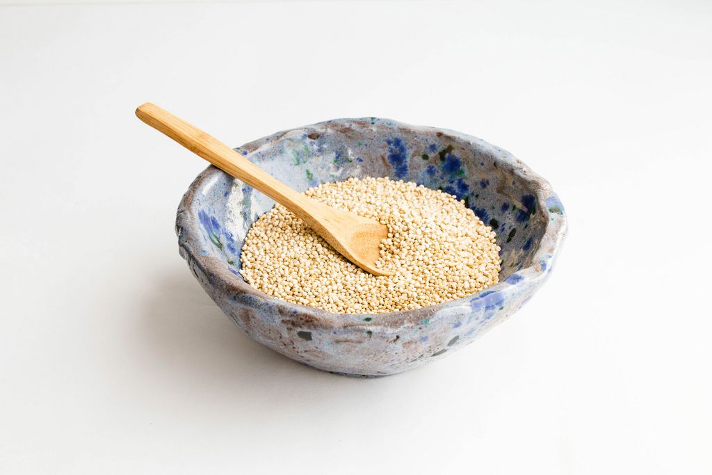 Ungekochte Quinoa Samen mit einem Holzlöffel in einer blauen Tonschüssel auf weißem Hintergrund