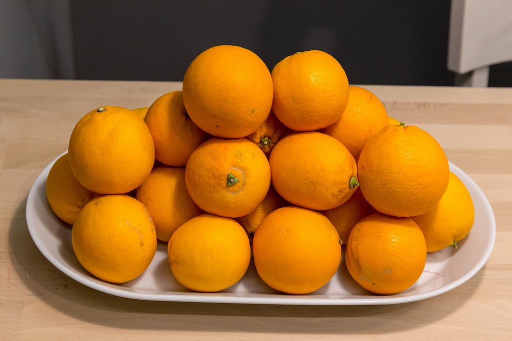 Ungeschälte Orangen gestapelt auf weißer Schale auf Holztisch