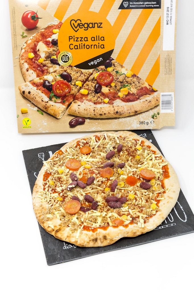 Vegan oven pizza on pizza stone plate next to pizza box