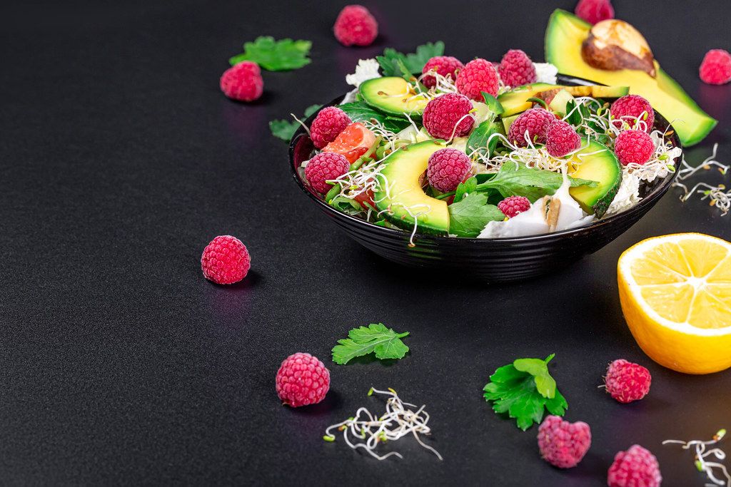 Vegetable salad with avocado, greens, onion micro-greens and raspberries on a black background