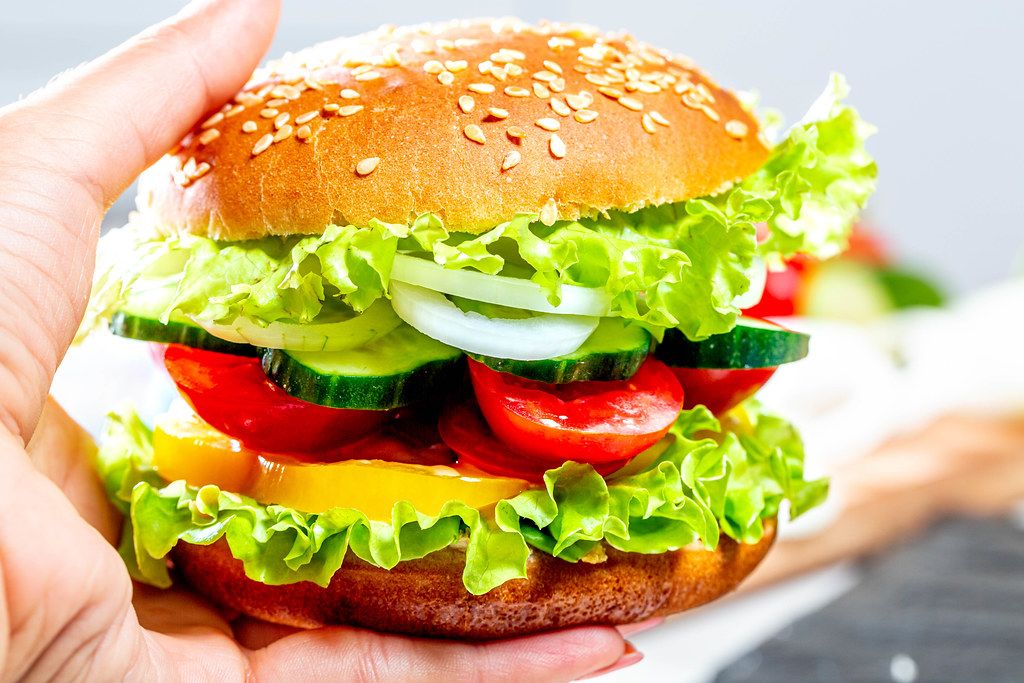 Vegetarian Burger with lettuce, cucumber, tomatoes, onions, bell pepper and sauce in a woman's hand