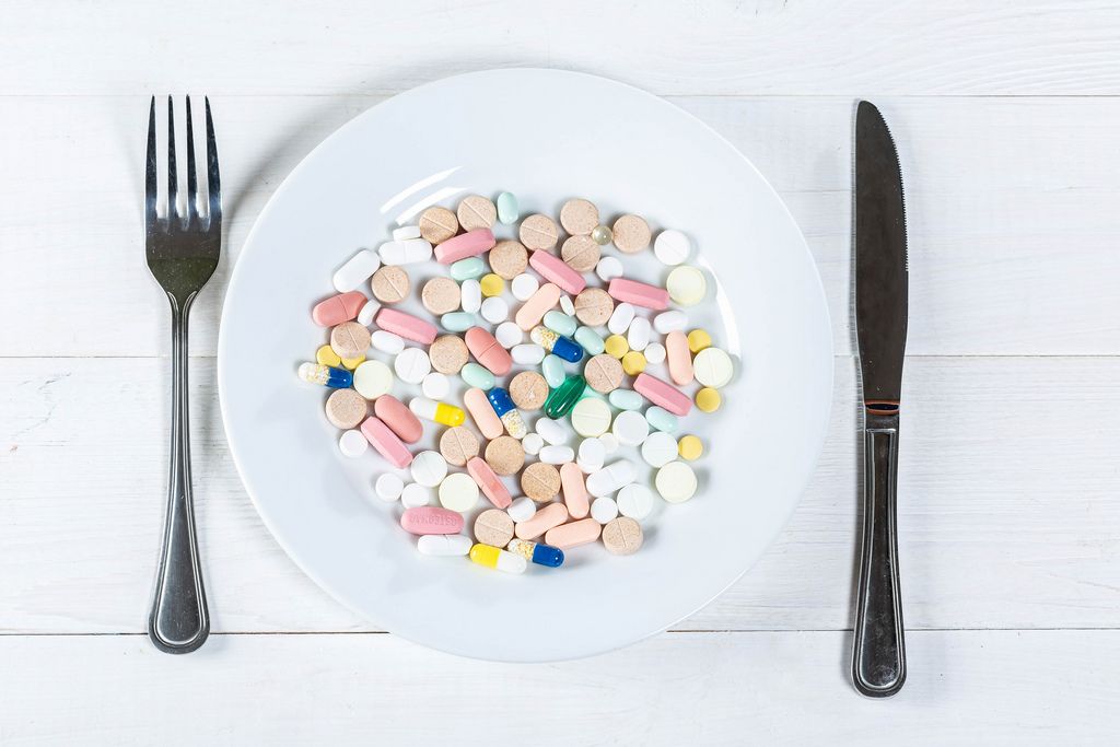 Verschiedene Pillen und Tabletten auf Teller mit Gabel und Messer auf weißem Holztisch