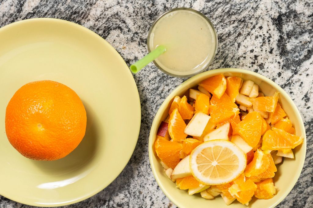 Vitaminreicher, gesunder Snack aus Obstsalat mit Äpfeln, Orange und Limonade auf Marmortisch