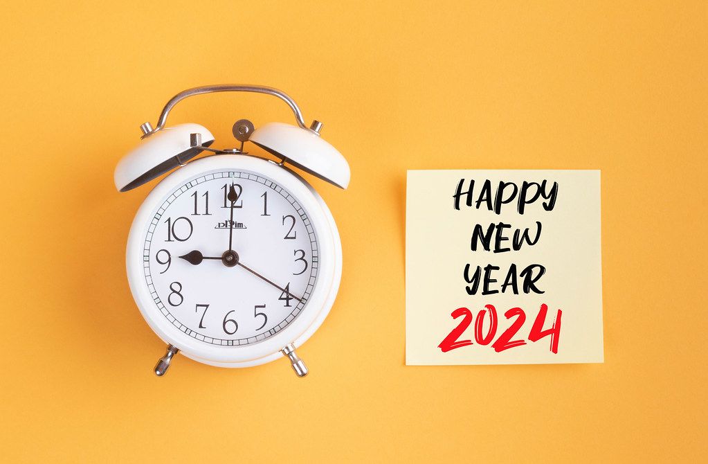 Wecker und ein Zettel mit ‘Happy new year 2024’ Text vor gelbem