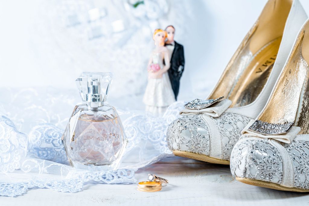 Wedding rings, perfume, shoes and statues of the bride and groom on white background