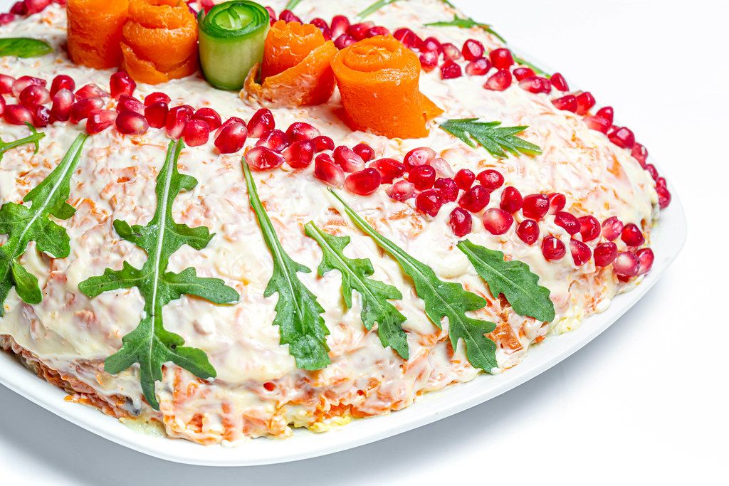 Weihnachtssalat dekoriert mit Rucola, Granatapfel-Kernen und Gemüse auf einem weißem Teller auf weißem Hintergrund