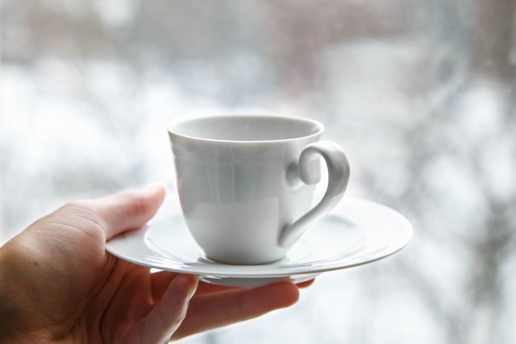 Weiße Kaffeetasse auf Unterteller in Frauenhand