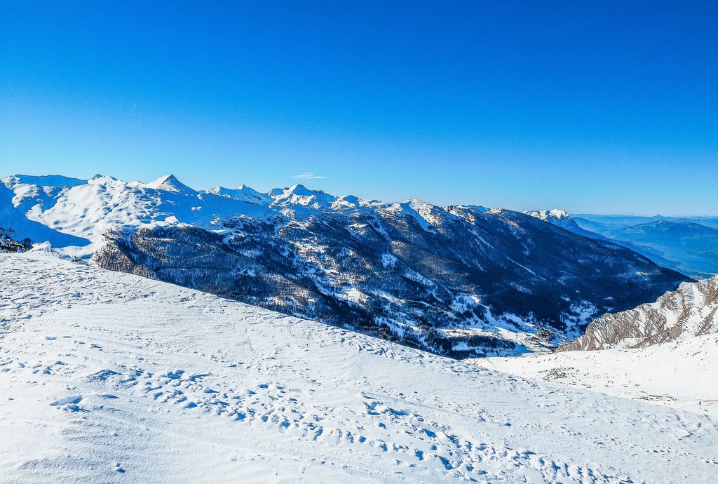 Weitblick von Gipfel über die umliegenden, verschneiten Berge bei Vars mit blauem Himmel