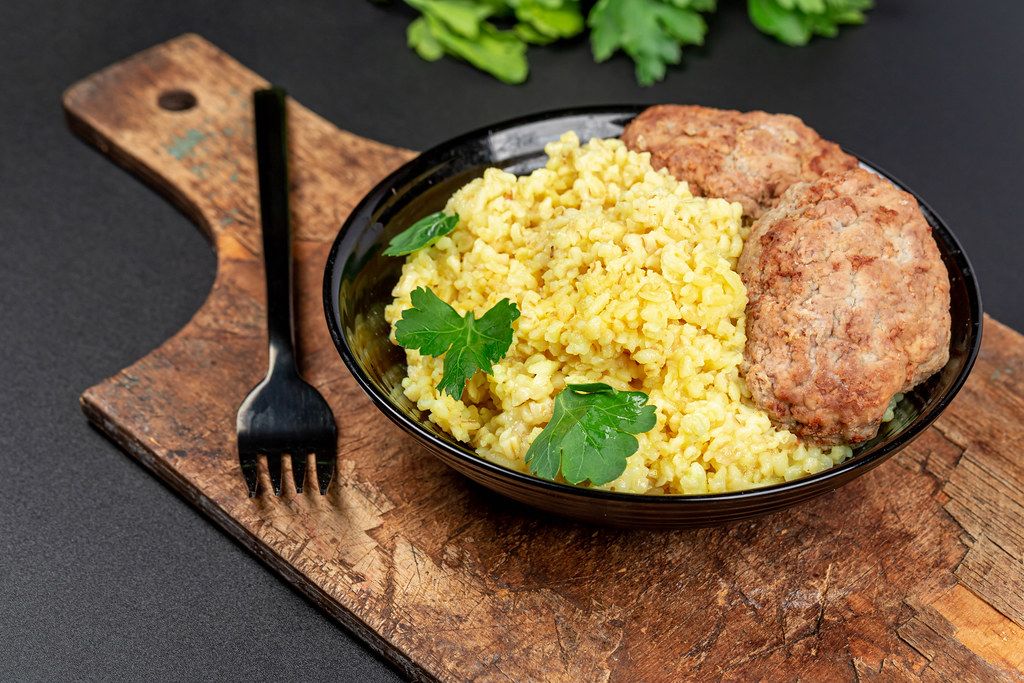 Wheat porridge with fresh parsley and cutlets on a dark background