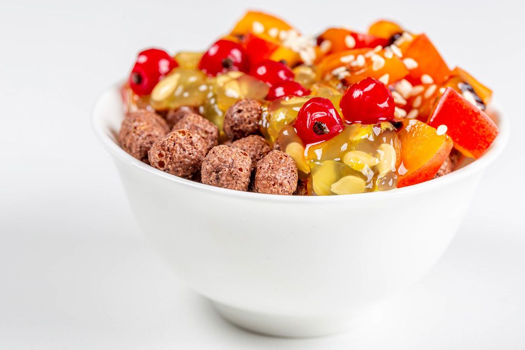 White bowl with corn balls and fruit on a white background