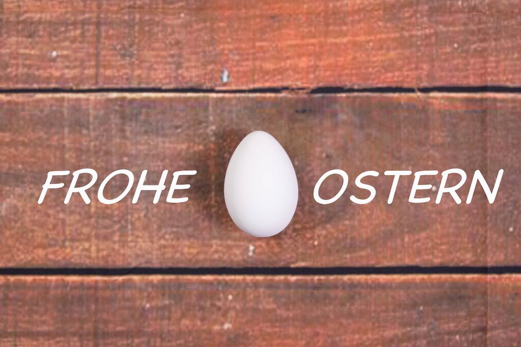 White chicken egg with Frohe Ostern text on wooden background