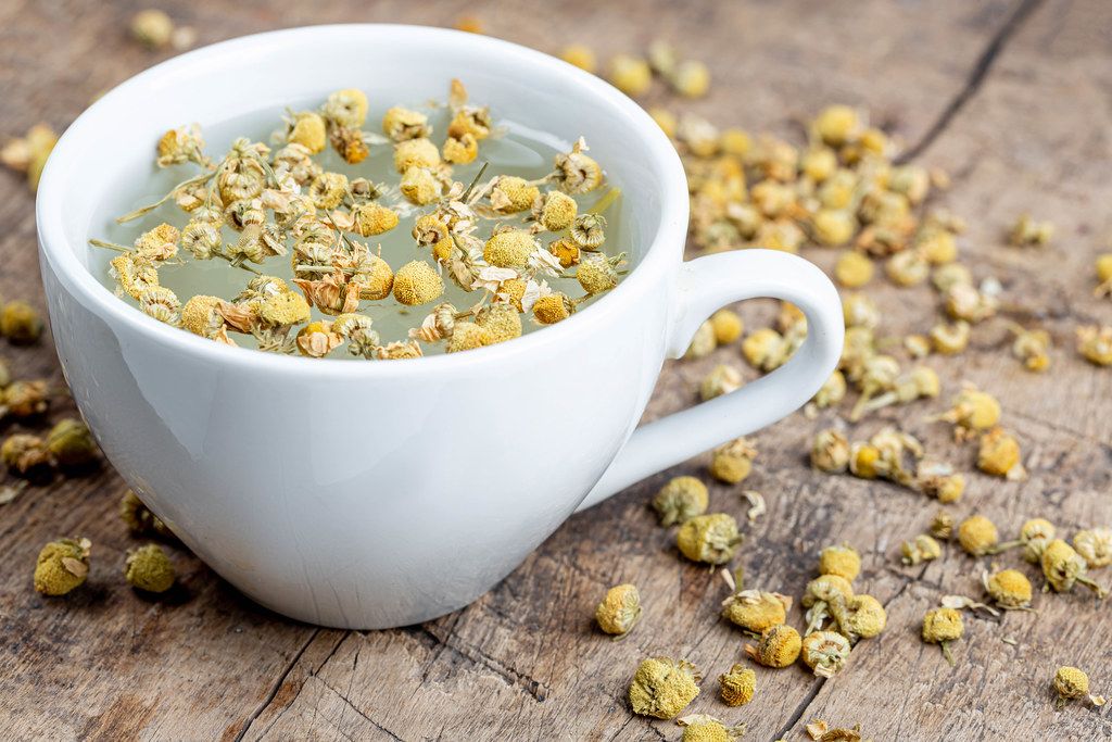 White cup of chamomile tea with dry chamomile flowers on a wooden background