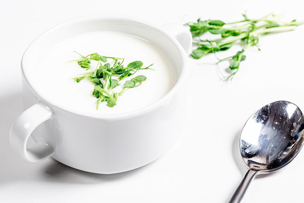 White mushroom soup with micro greenery and spoon on white background