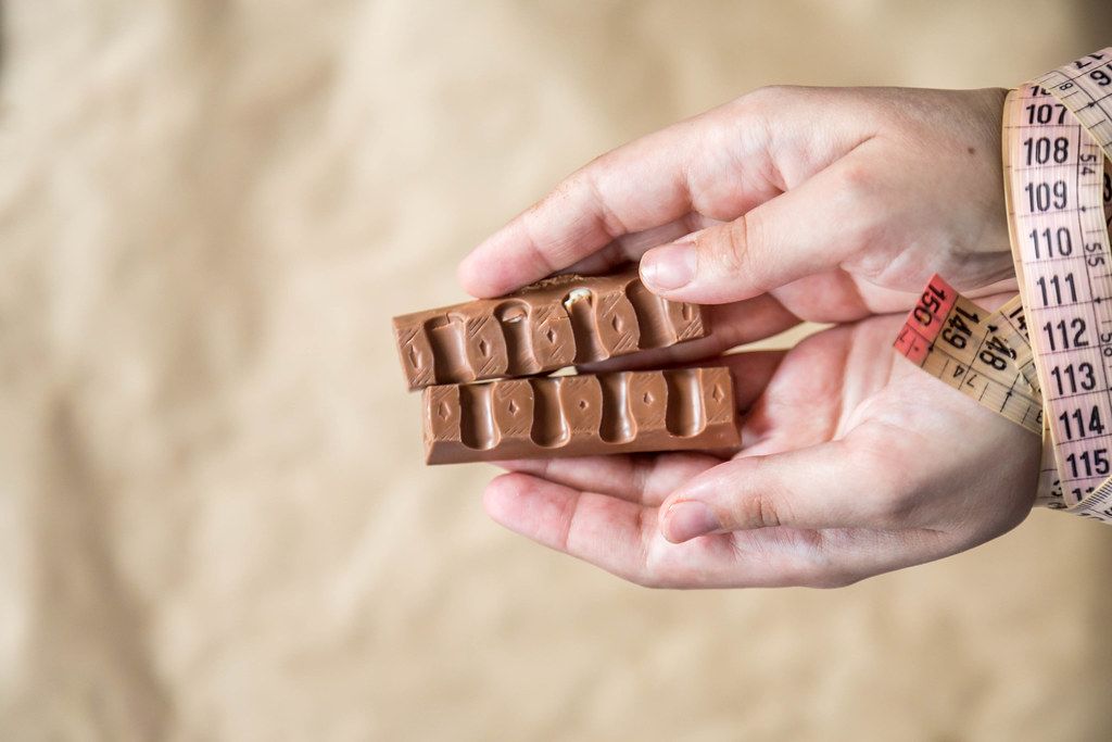 Woman hand bounded with measuring tape holding slices of sweet chocolate. Diet concept.