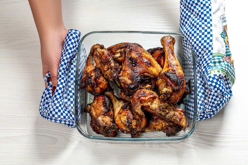 Woman holds potholders glass baking tray with baked chicken pieces (Flip 2019)